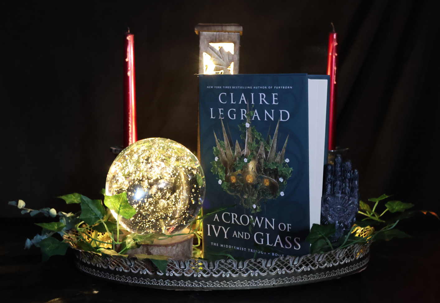 A Crown of Ivy and Glass book, framed by a lit crystal ball, candles, incense, and green ivy.