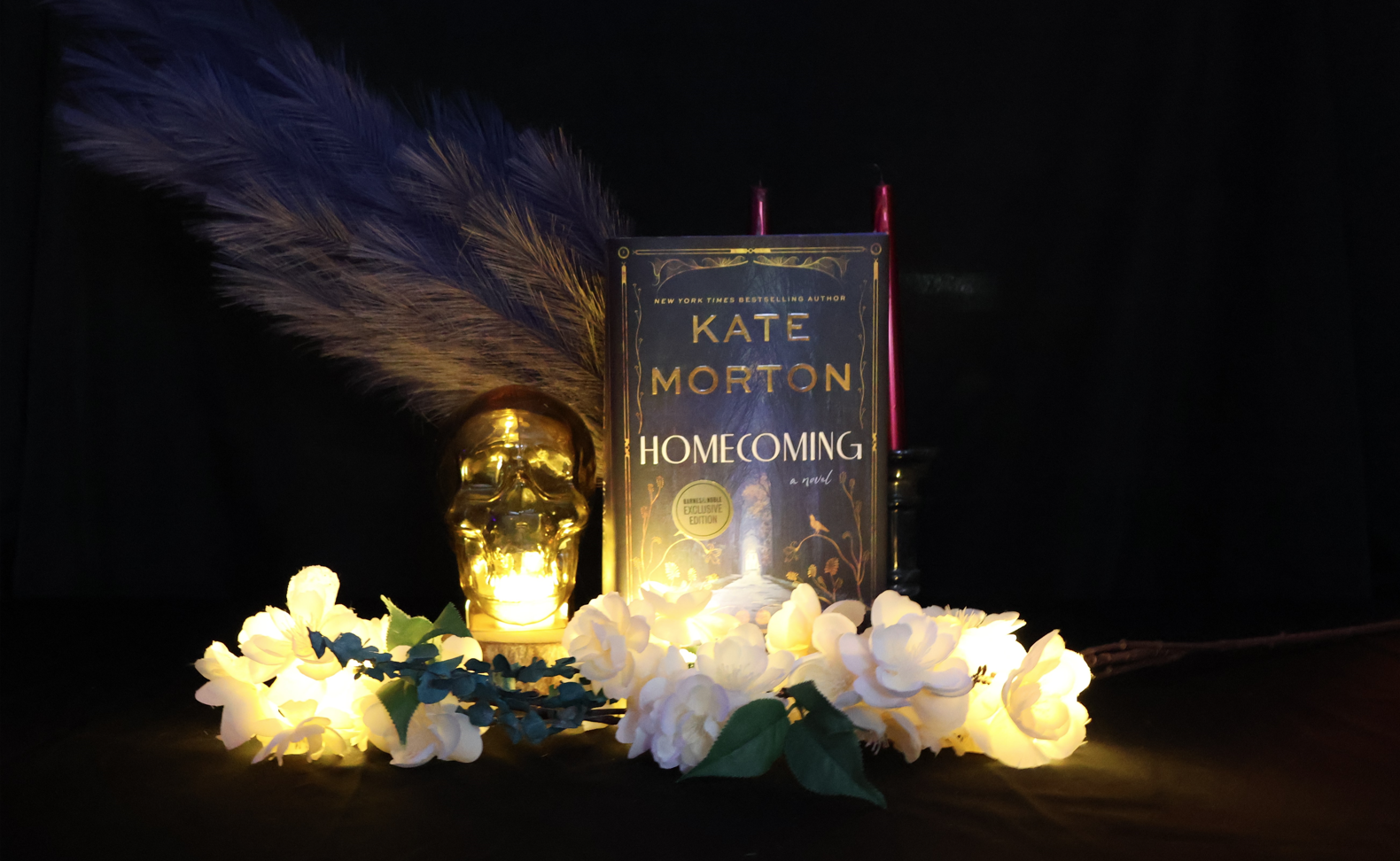 Homecoming book, framed by candles, florals, feathers, and an internally lit glass skull.