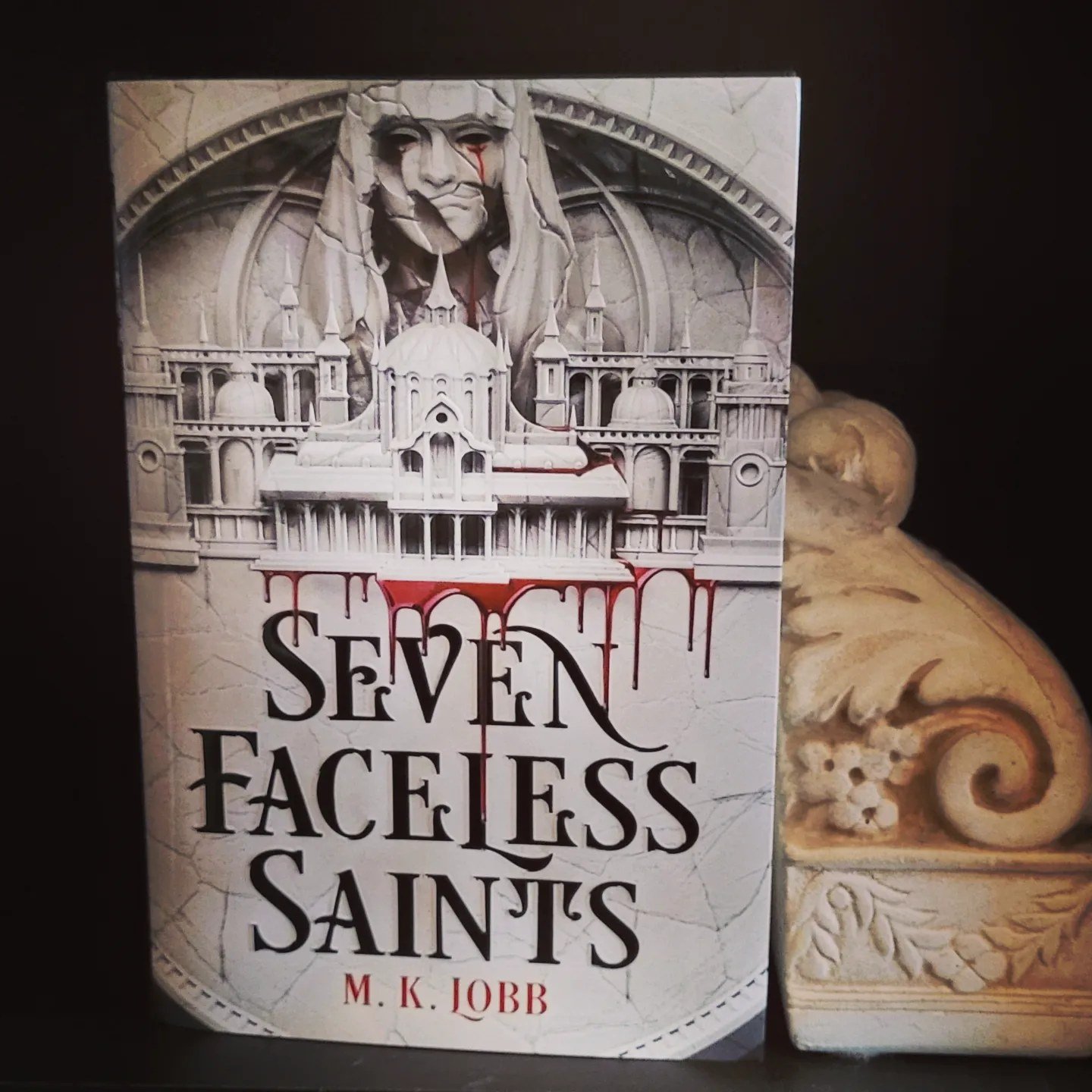 The Seven Faceless Saints book, framed by a carved floral bookend.